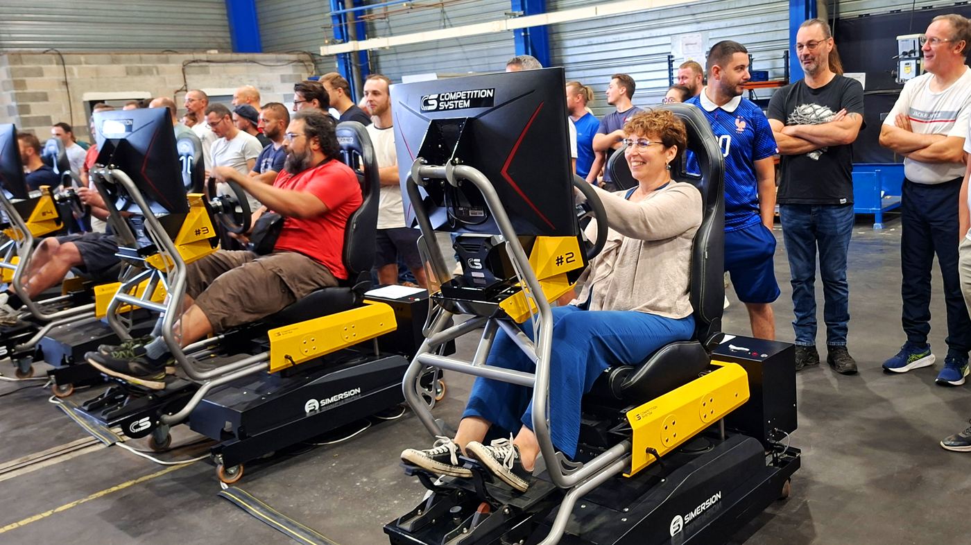 Participante souriante au volant, collègues autour des simulateurs